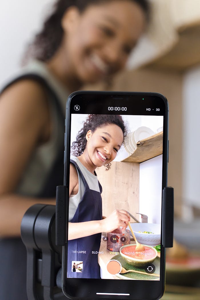 our-story Smiling woman filming cooking video on smartphone in kitchen.